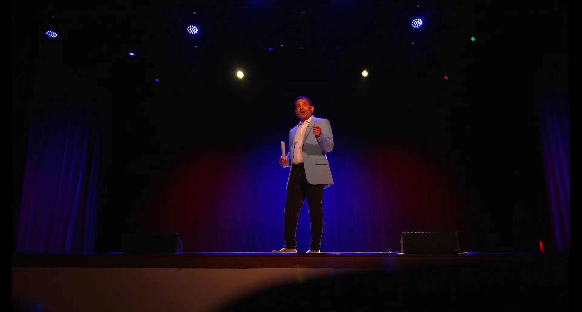 Nik Agharkar presenting on stage under a spotlight